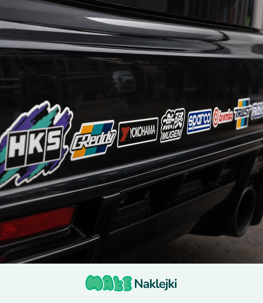 Rząd naklejek tuningowych z logotypami marek motoryzacyjnych naklejonych na czarnym zderzaku samochodu sportowego.